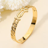 Gold-tone stainless steel sculptural interlock hinged bangle bracelet featuring chain-inspired detailing and a polished modern design on a beige background