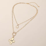 Gold layered necklace featuring a textured cross pendant, round stone charm, and mixed paper clip chain design on a beige background