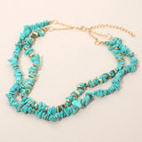 Double layered turquoise natural stone chip bead necklace with gold dipped accent beads and adjustable clasp on a beige background