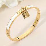 White enamel hinged bangle bracelet with gold-tone stainless steel finish and lock charm accent on a beige background